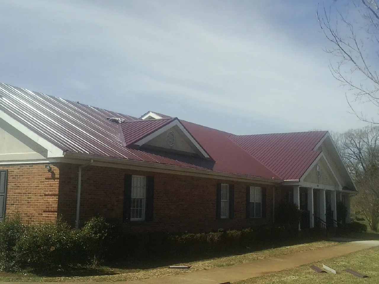 Red metal roof with gabled entries on a long brick building, from a Hail Damage Roof Repair job in Archbold