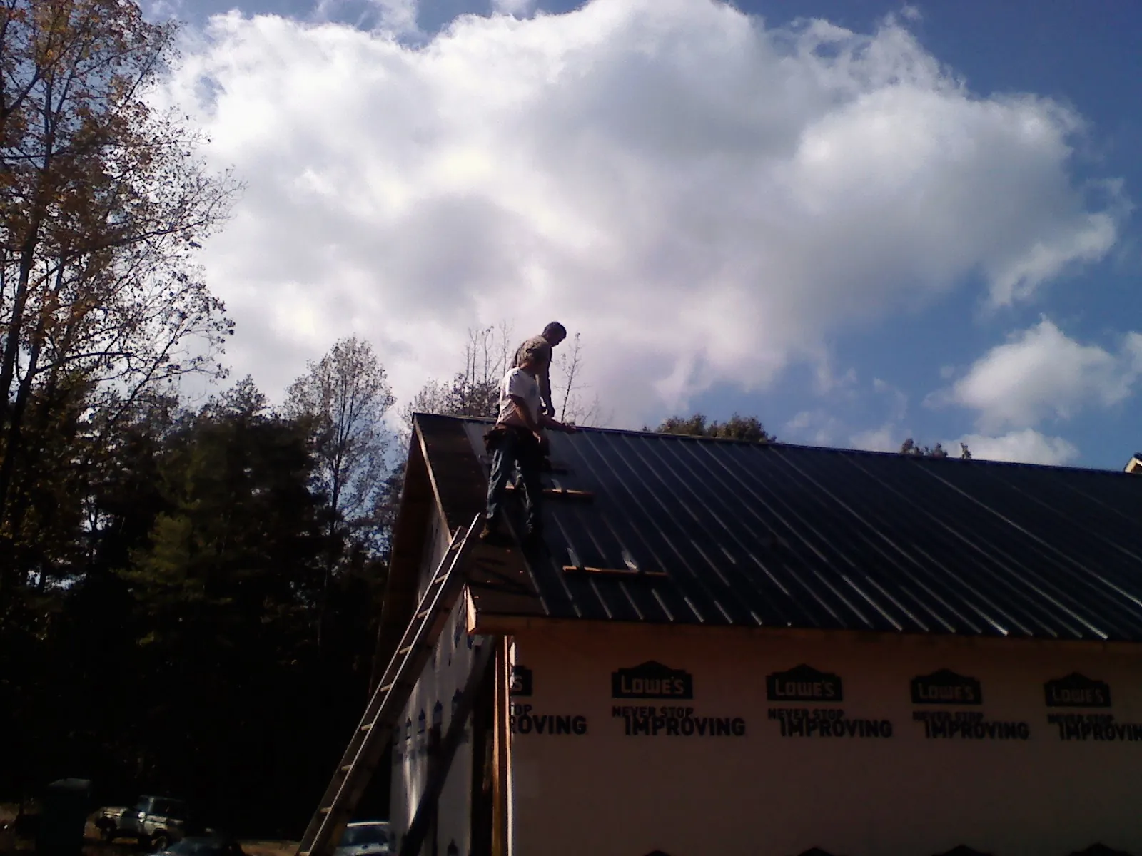Roofer fastening dark metal panels high against a cloudy sky, from a Roof Inspection job in Archbold