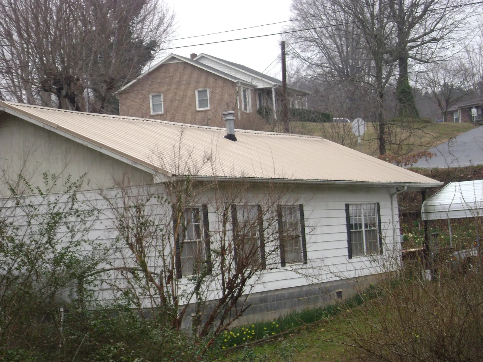 Tan metal roof on a white sided house set into a hillside — Commercial Roofing by Roofing Brothers in Archbold